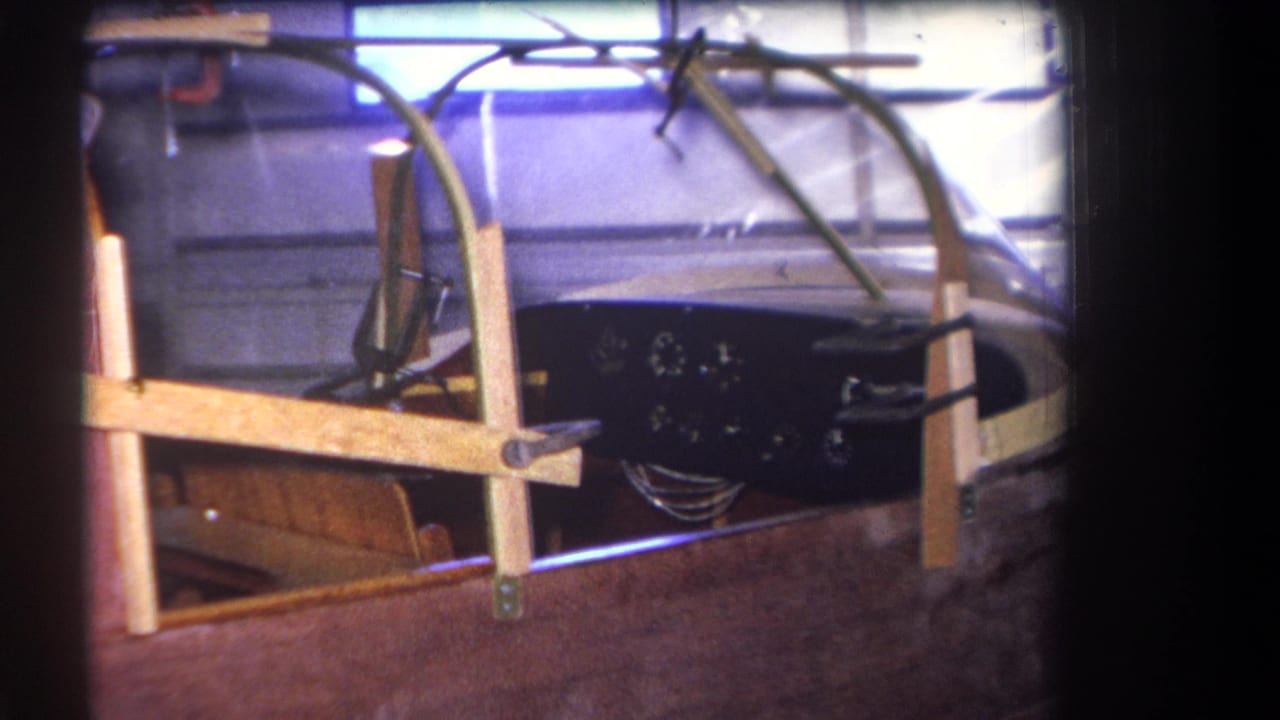 Classic wooden boat cockpit with dashboard, gauges, windshield frame, and seat visible in a garage.