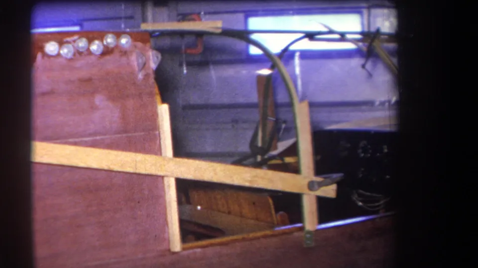 1964 8mm frame showing the varnished wooden boat deck and cockpit details, including chrome fittings, windshield support, dashboard edge, and seat.