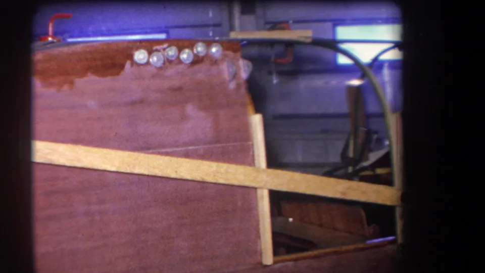 1964 home-movie frame from Yucaipa-area footage showing the boat's varnished deck, chrome hardware, windshield support, and partially visible cockpit seat.