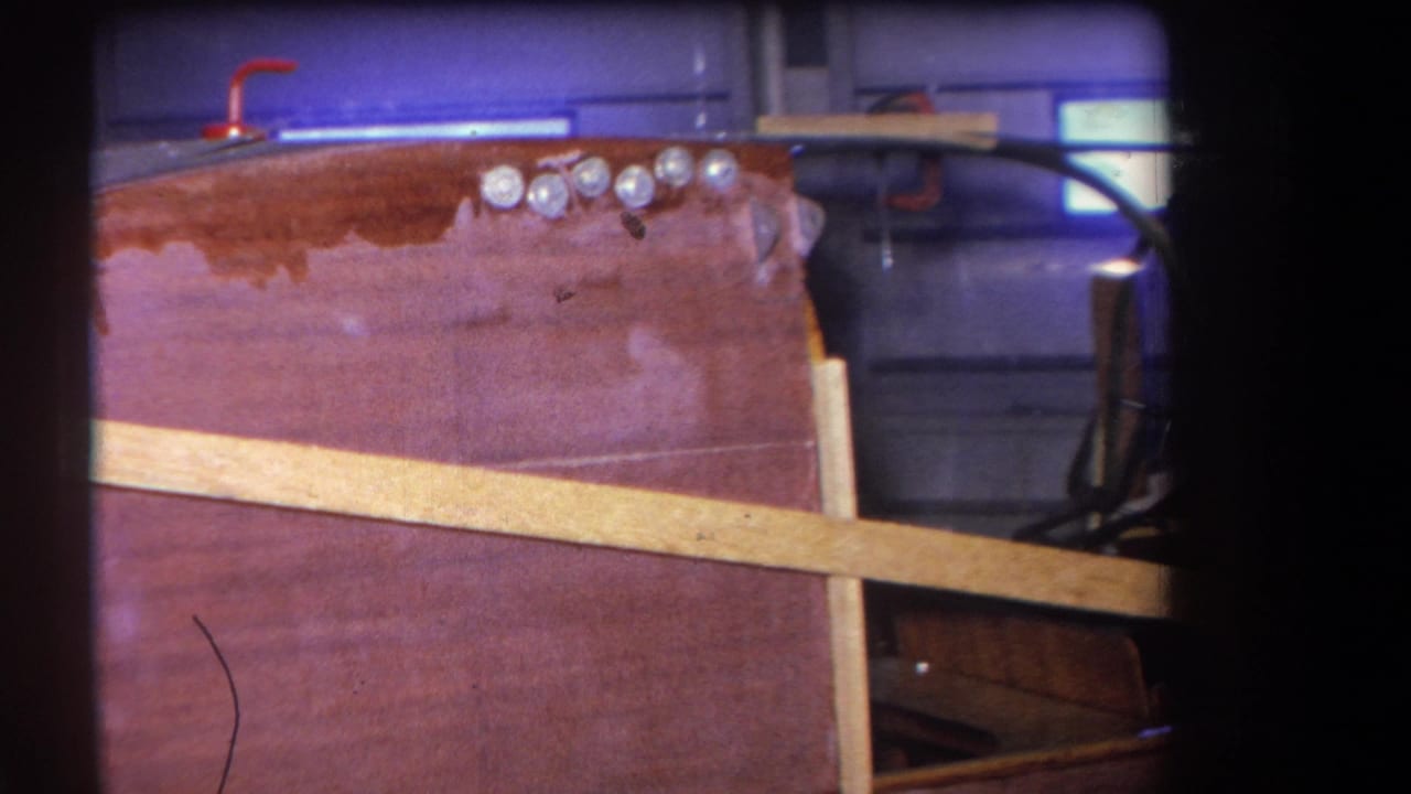 Close view of an unfinished wooden airplane fuselage side with pale bracing and silver fasteners.