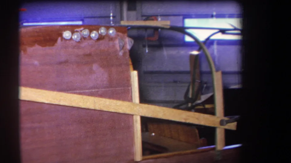 1964 Yucaipa workshop frame showing a partly built wooden aircraft fuselage with pale braces, fasteners, and exposed interior support pieces.