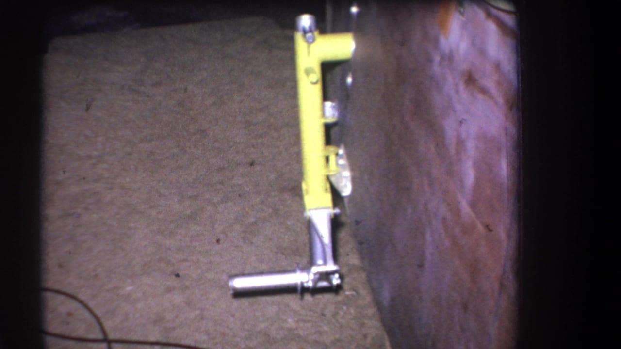 1964 home-movie frame from Volmer Yucaipa, California, showing a yellow mechanical object with a metal handle beside rough wooden boards.