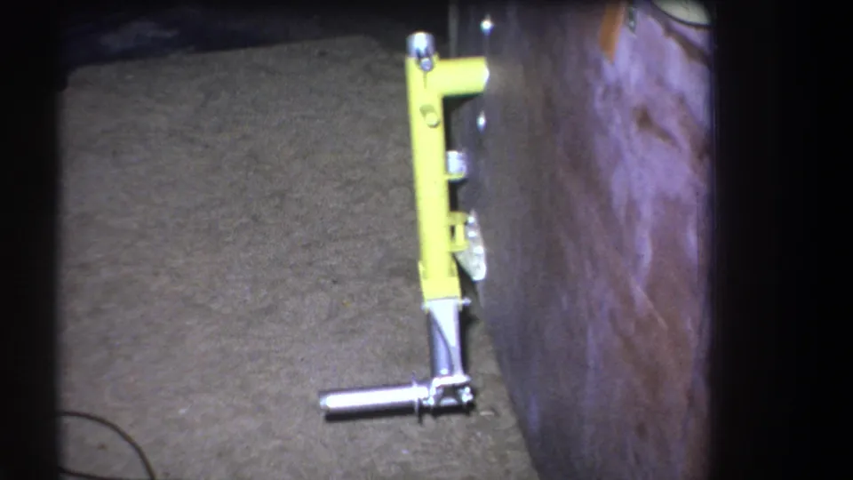 Final 1964 frame holds on the yellow mechanical object beside the wooden surface, with dark 8mm frame edges and grain visible.