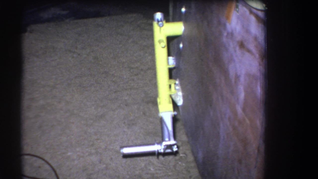 A close home-movie view of a yellow wall-mounted tool with silver hardware inside a likely workshop or garage setting.