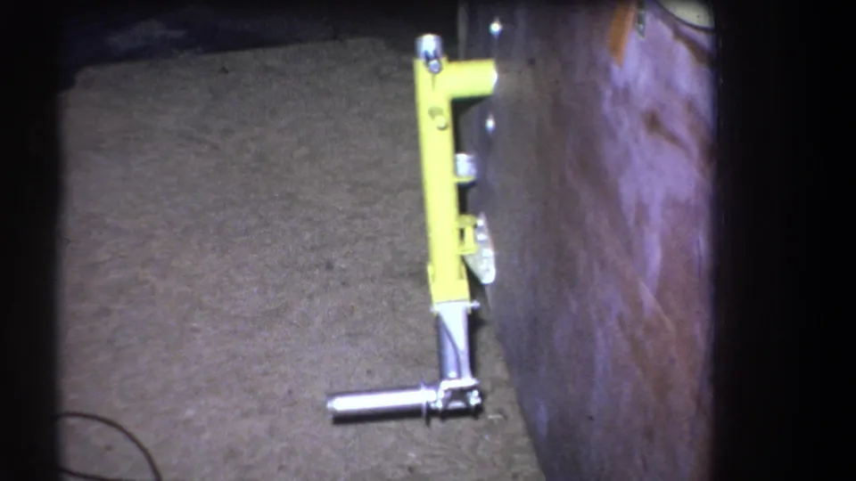 1964 archival frame showing the yellow tool from a similar angle, emphasizing the mounted bracket and low metal handle.