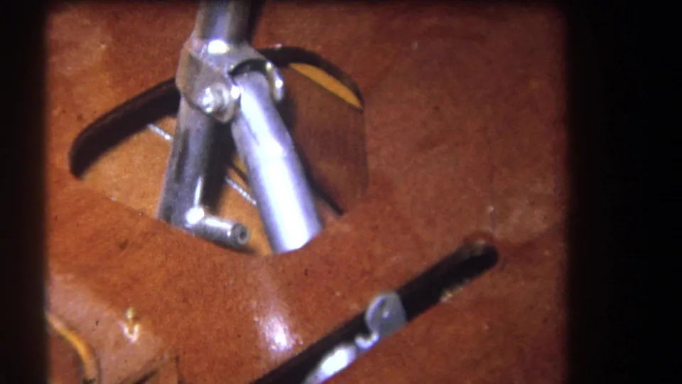 Close home-movie detail of silver lever hardware and dark handles resting against a reddish wood surface in the same clip.