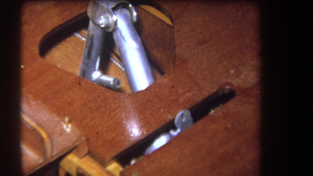 Close-up of varnished wood with silver metal fittings and a dark slotted opening.