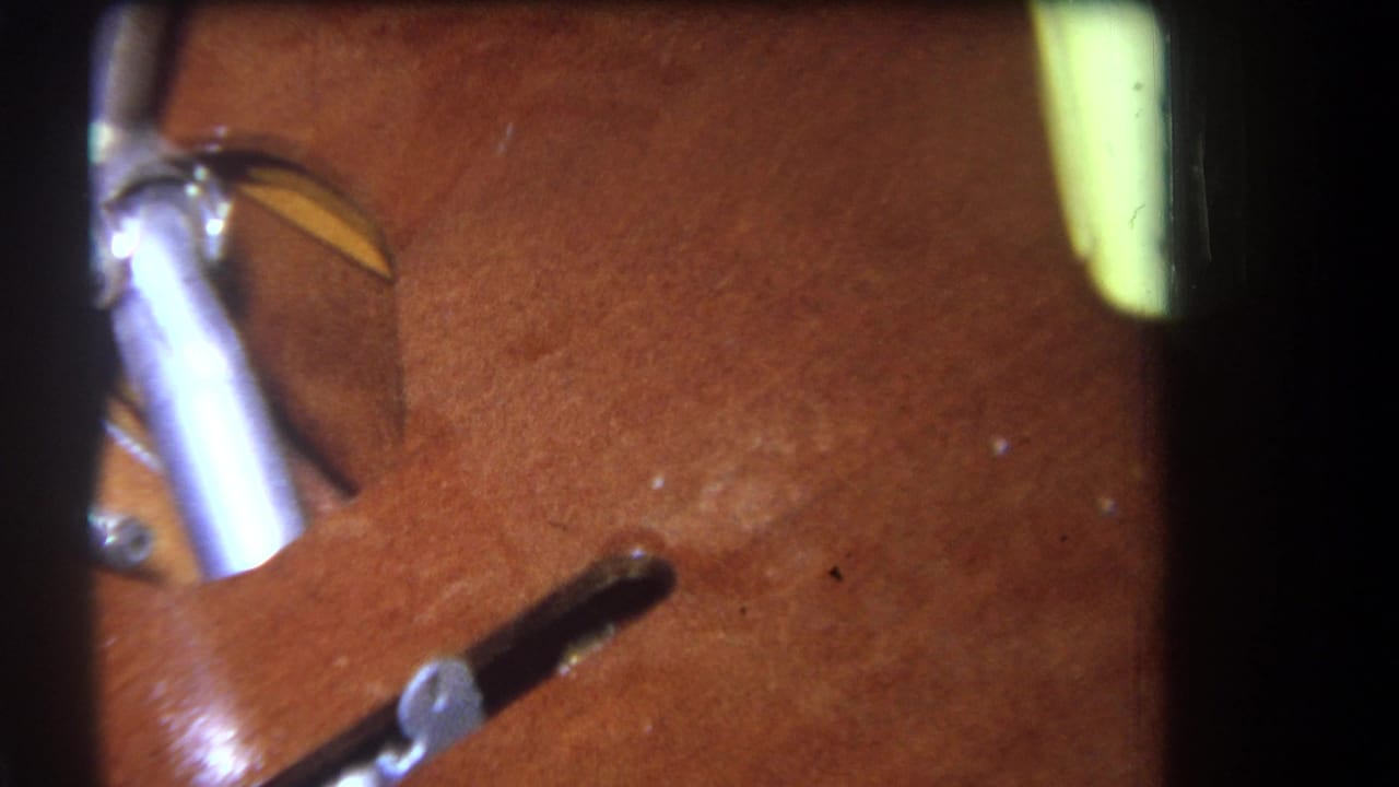 Close 1964 home-movie frame of a wooden structure with a silver metal part, dark opening, and pale yellow object at the edge.
