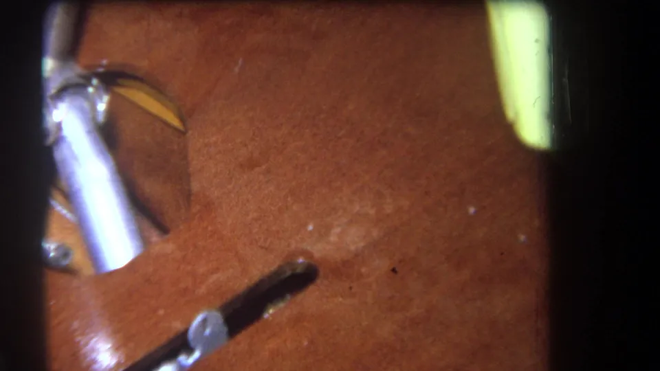 Close 1964 home-movie frame of a wooden structure with a silver metal part, dark opening, and pale yellow object at the edge.