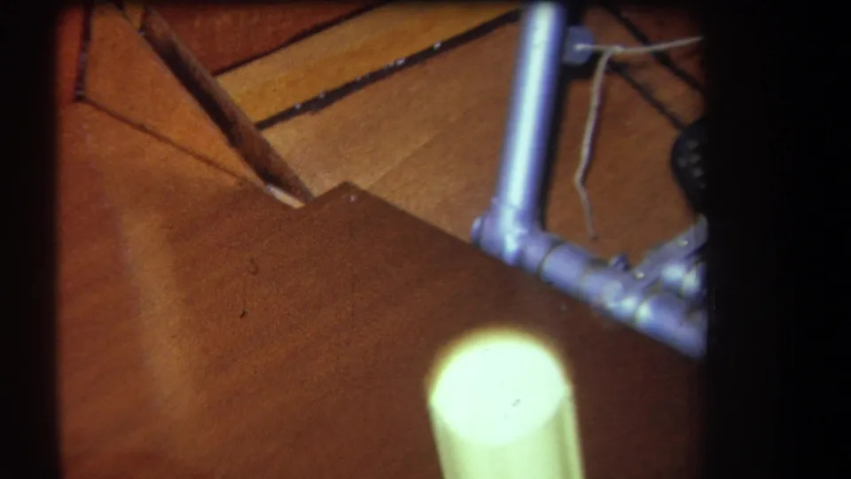 Close 1964 Yucaipa frame showing wooden panels, silver rod-like fittings, and a pale yellow cylinder inside the structure.