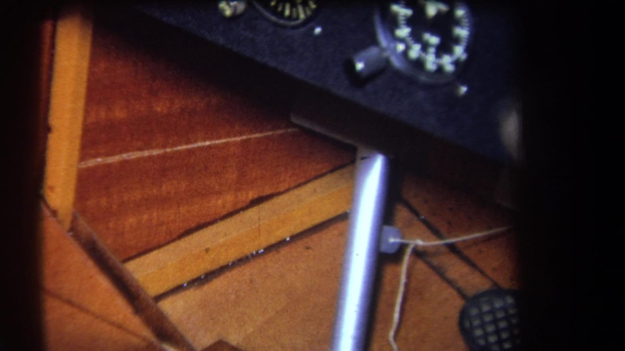Close 1964 home-movie view of a small aircraft cockpit, with the control stick below a dark analog instrument panel.