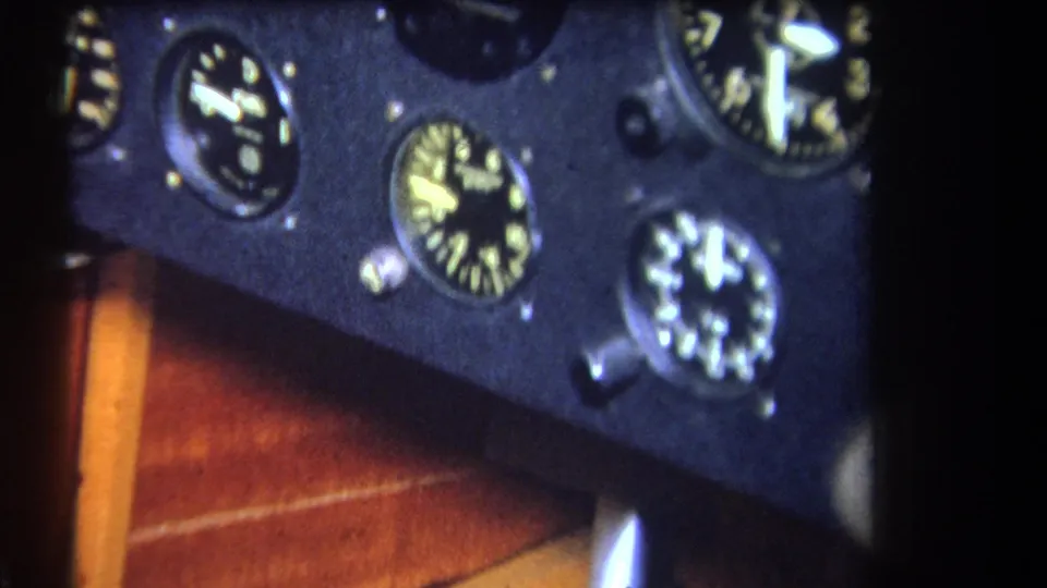 1964 8mm cockpit detail showing a dark instrument panel with multiple analog gauges and warm wooden trim at the edge.