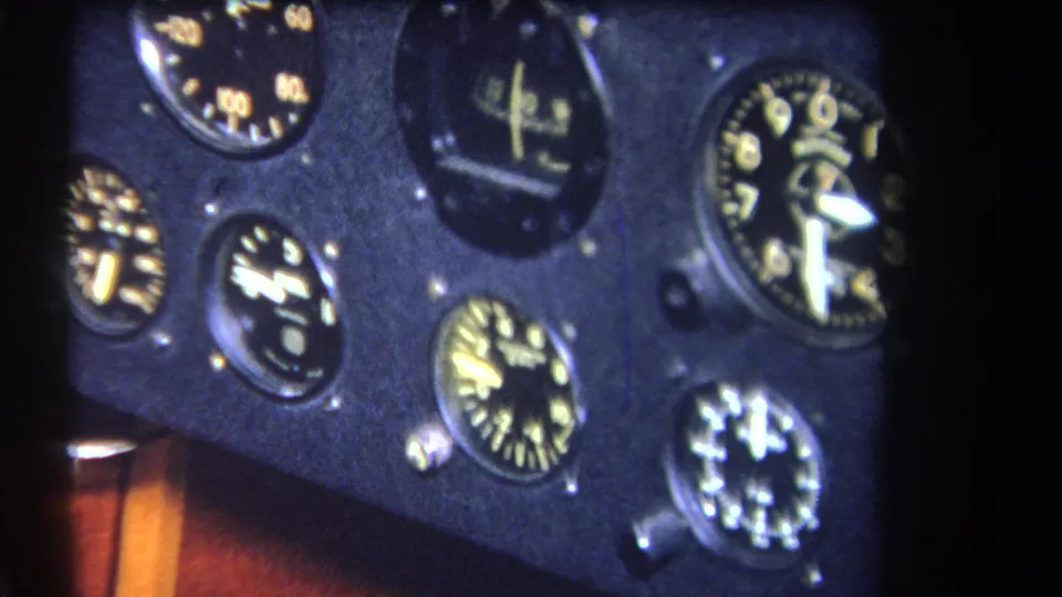 Close 1964 home-movie frame of a small aircraft instrument panel, showing several round gauges with yellow markings.