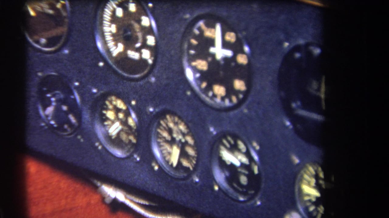 Close 1964 home-movie view of analog aircraft gauges on a dark panel, framed by black film edge and a glimpse of wood trim.