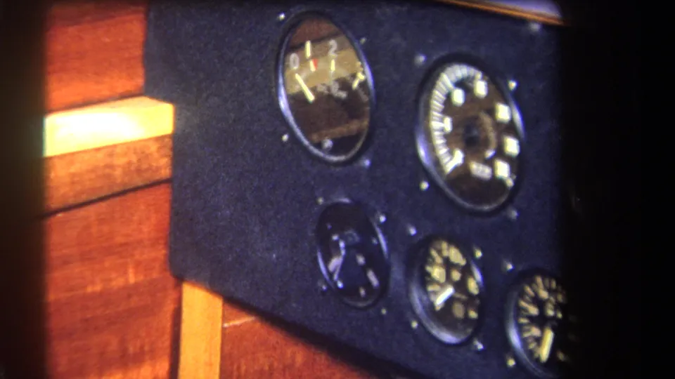 End frame of a 1964 aircraft cockpit detail, showing round analog gauges on a dark panel with wood trim and soft 8mm focus.