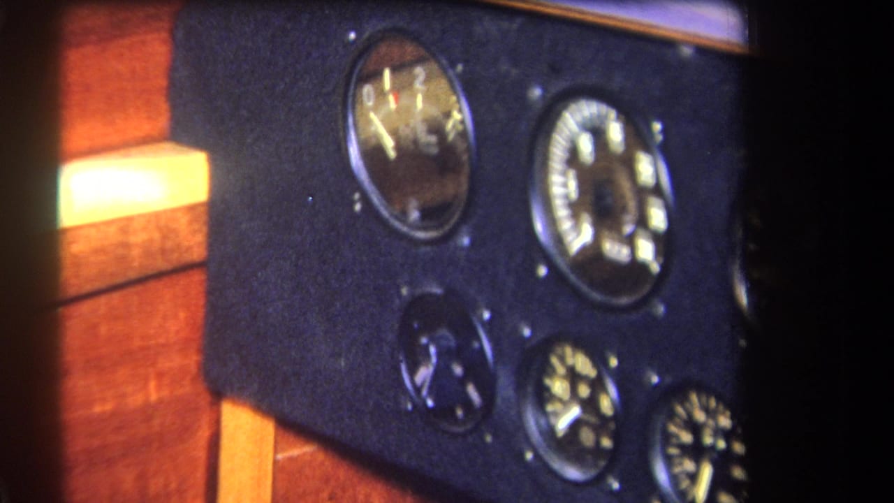 1964 8mm frame showing a dark vehicle or machinery instrument panel with round analog gauges and warm wood-grain cabin surfaces.
