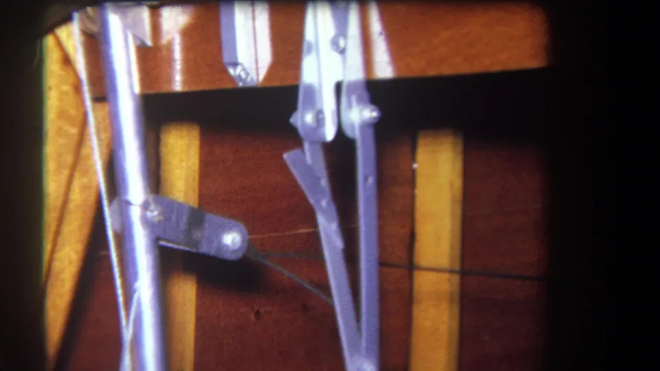 1964 8mm frame showing silver mechanical linkage components, a cable, and wood paneling inside a vehicle or machinery cabin.
