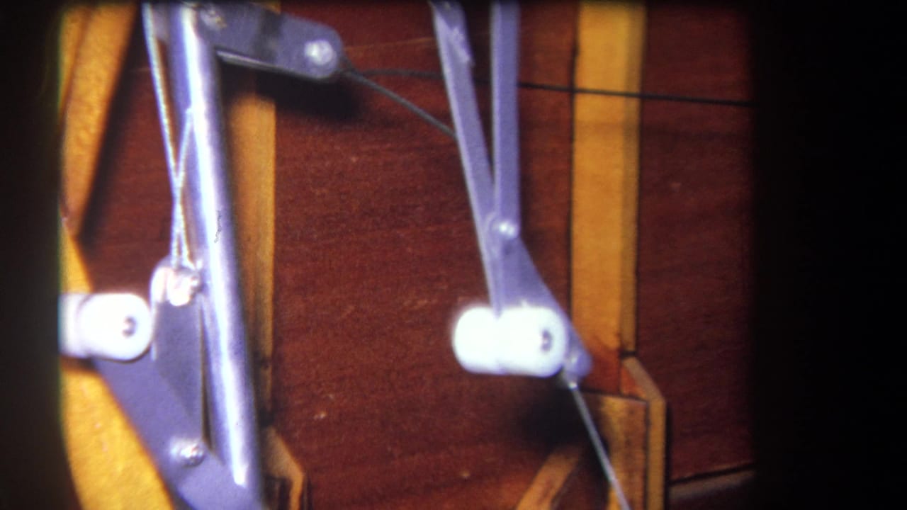 Close view of painted metal arms, white rollers, wire cable, and wooden panels.