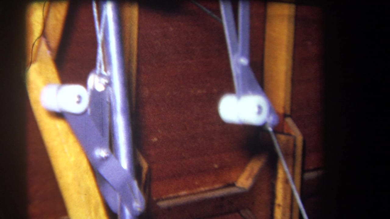 Close 8mm frame of the wooden apparatus with purple linkage, white roller parts, rods, and dark scan borders.