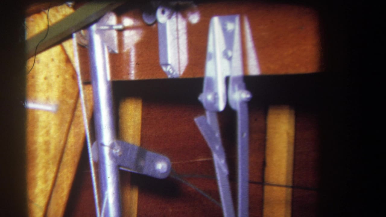 1964 Yucaipa-area 8mm frame showing silver mechanical rods, brackets, and clamps stored against brown wood and yellow material.