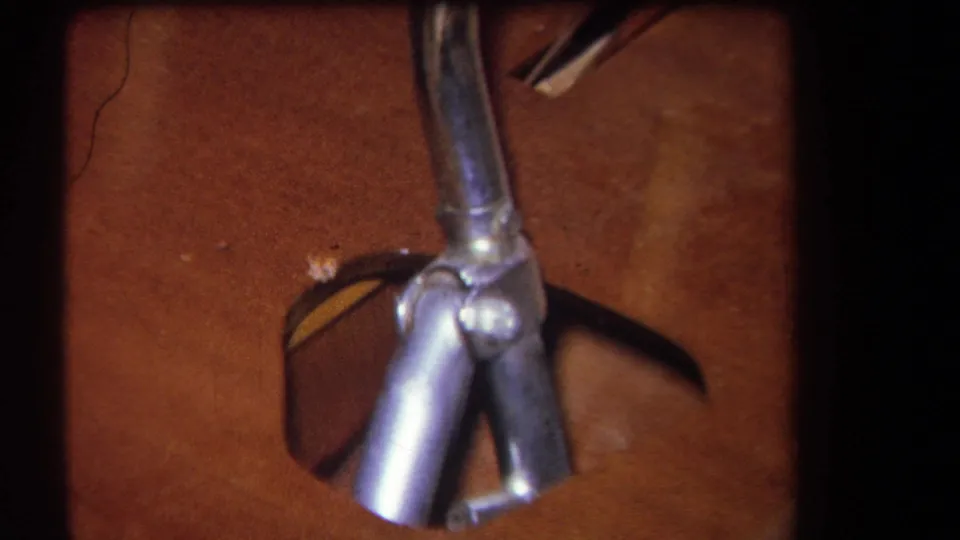 1964 Yucaipa-area 8mm frame showing tubular metal pieces and joints near a brown wooden surface with dark straps or cords.