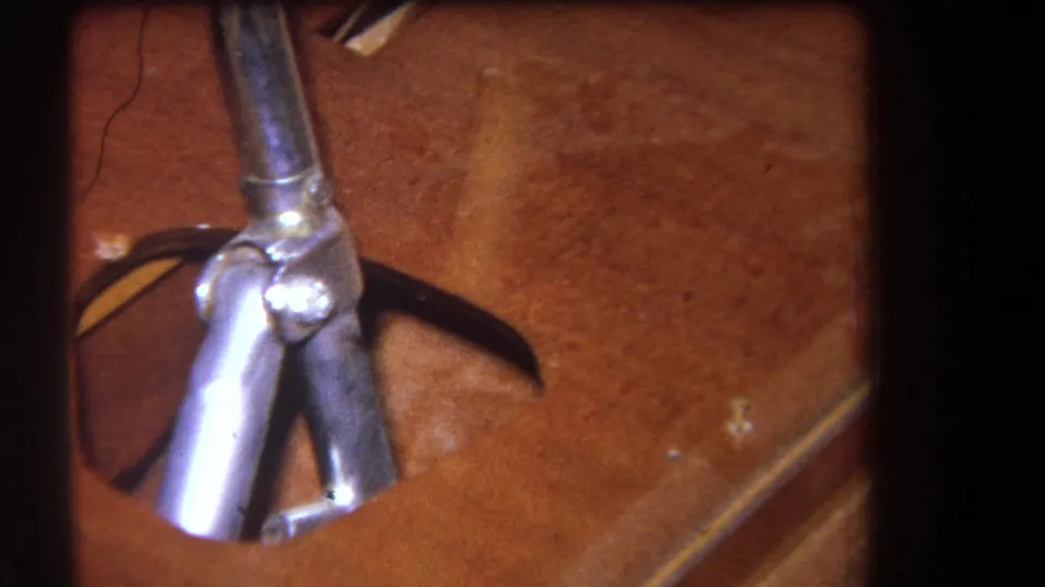 1964 Yucaipa-area 8mm frame focused on a shiny metal joint and tubular rods resting against a brown wooden surface.