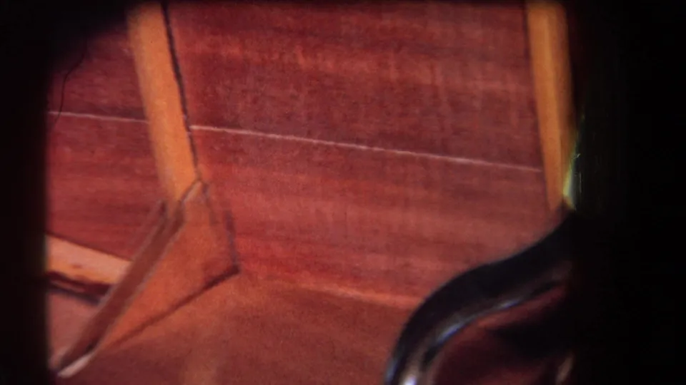 1964 8mm close-up of angled wood joinery and paneling, with part of a dark pipe entering the lower frame.