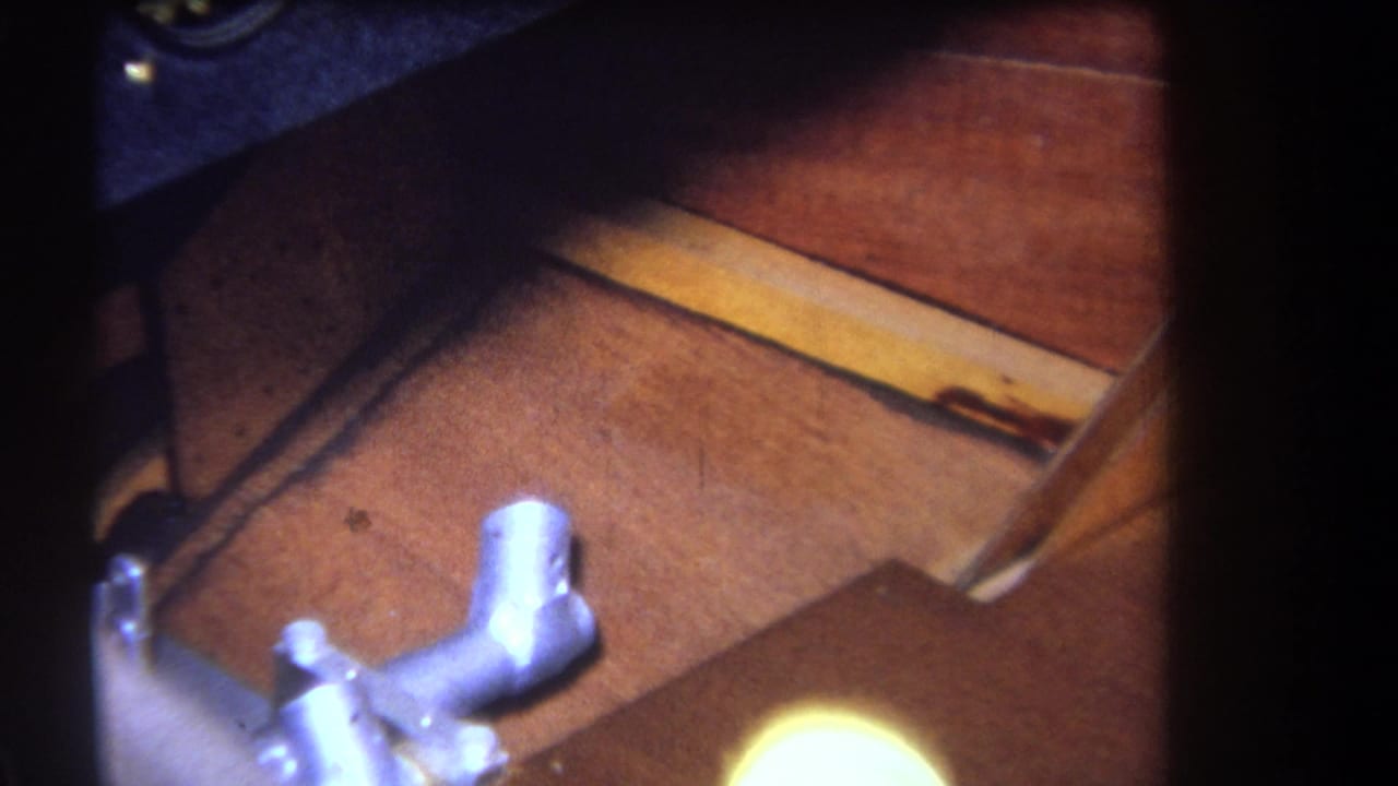 1964 Yucaipa-area home-movie frame showing a small aircraft cockpit floor, metal control lever, and dark instrument panel edge.