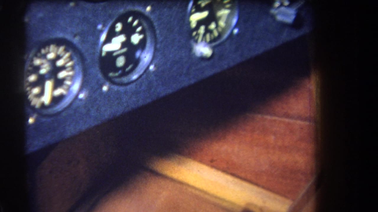 1964 Yucaipa-area home-movie frame showing a dark cockpit instrument panel with round analog gauges over wood-toned flooring.