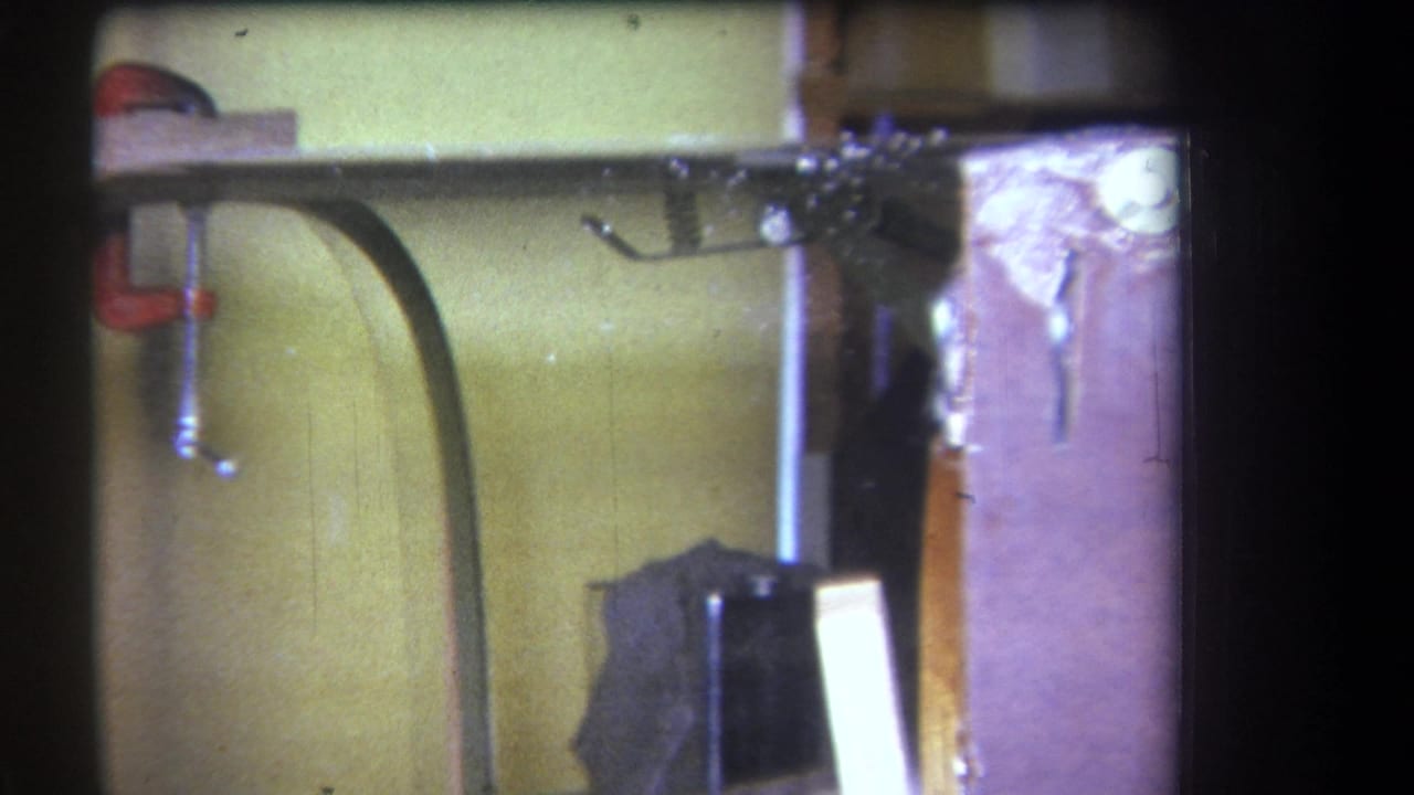 Close view of a workshop wall with clamps, hose, vertical boards, and a wooden frame edge.