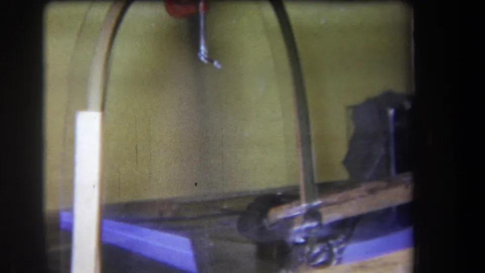 1964 Yucaipa-area 8mm frame showing the experimental-looking workshop arrangement from closer range, with curved wood, a red clamp, cable, and metal parts.
