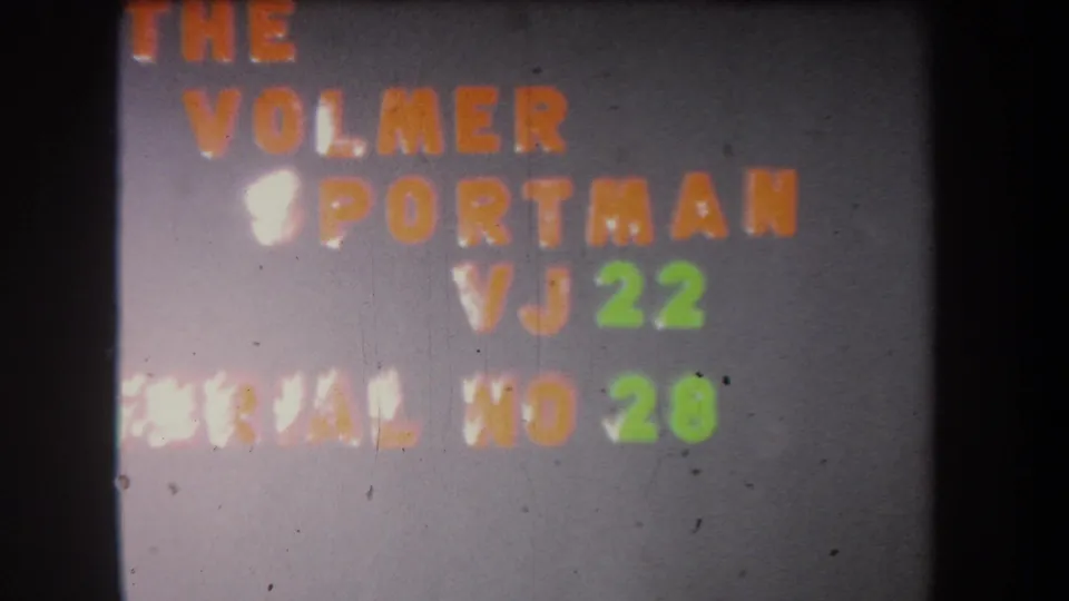 Soft, flickering 1965 8mm title-card frame showing The Volmer Sportman VJ 22 and serial number text in orange and green.