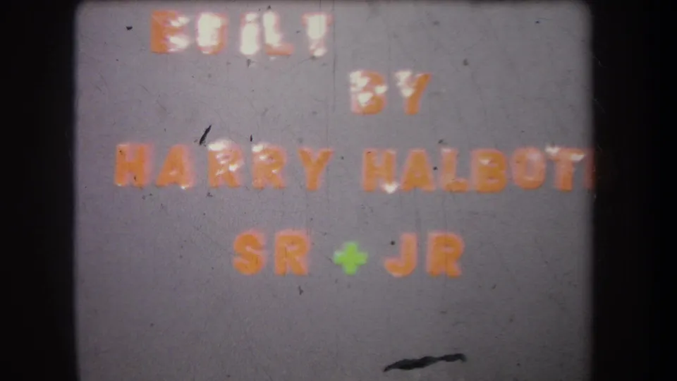 1965 8mm frame shows the Harry Halbott Sr + Jr production credit card with dust, scratches, and dark projector borders.