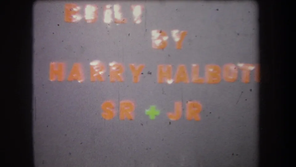 Final 1965 8mm contact-sheet frame of the Harry Halbott Sr + Jr title card, with gray field, orange text, and film wear.
