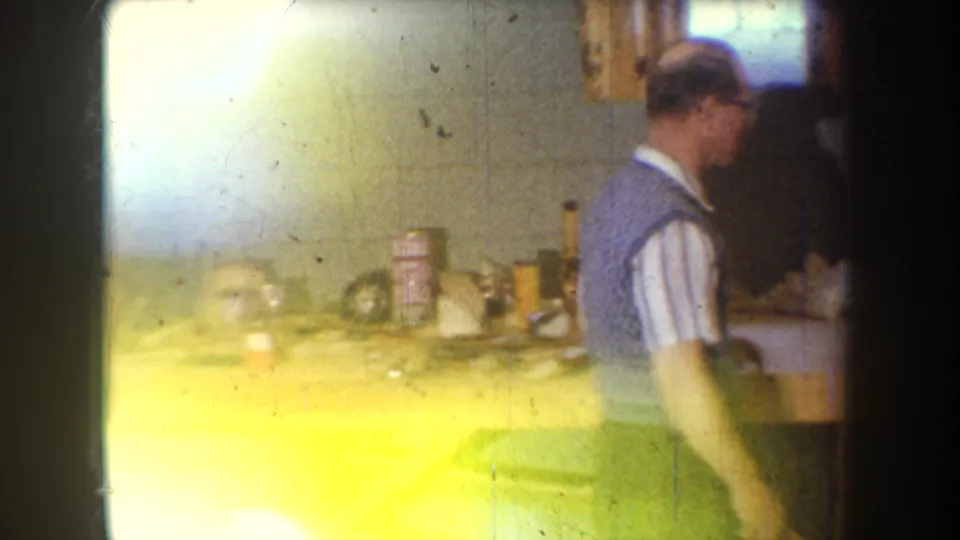 In a private Yucaipa-area interior, a man stands near a workbench with tools and containers in soft 8mm light.