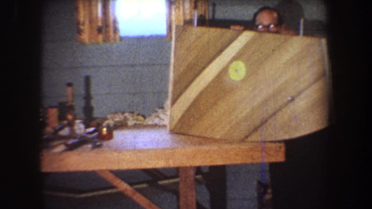 1965 Yucaipa workshop frame with a man in glasses partly hidden behind a curved wooden construction on a bench.