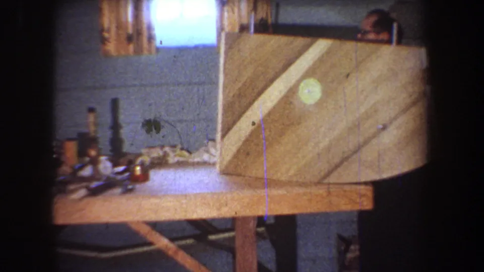 1965 Yucaipa 8mm frame showing a private workshop bench, curved wooden panel and a partially visible man behind the construction.
