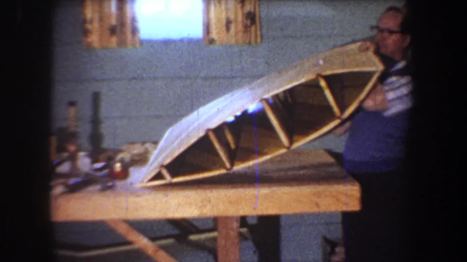 The man in glasses supports the angled wooden hull, showing its ribbed interior in the 1965 workshop footage.