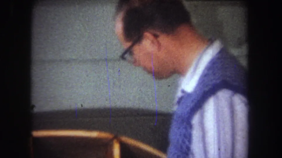 1965 home-movie frame from Yucaipa showing a man in glasses and a blue sweater near the wooden model boat.