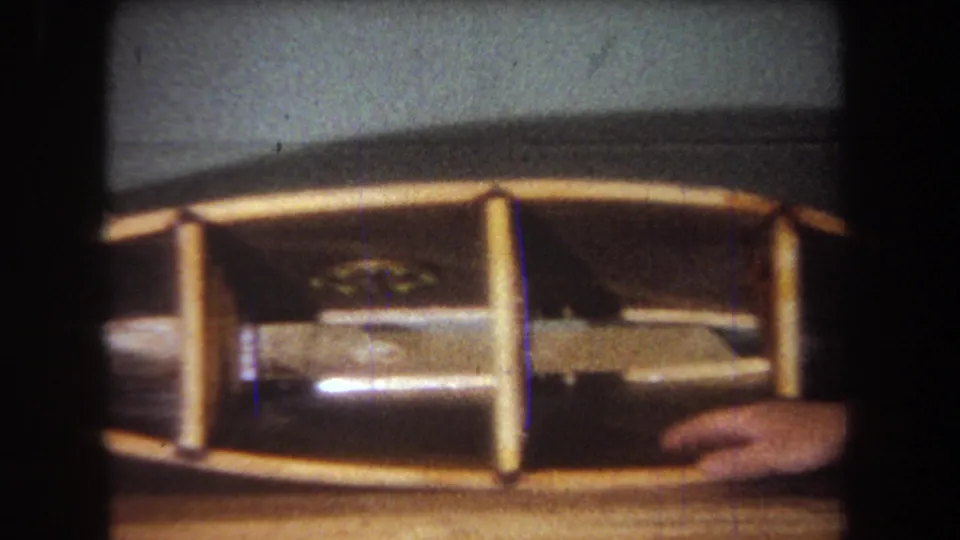 1965 Yucaipa frame showing a wooden model boat held steady in a close domestic home-movie shot.