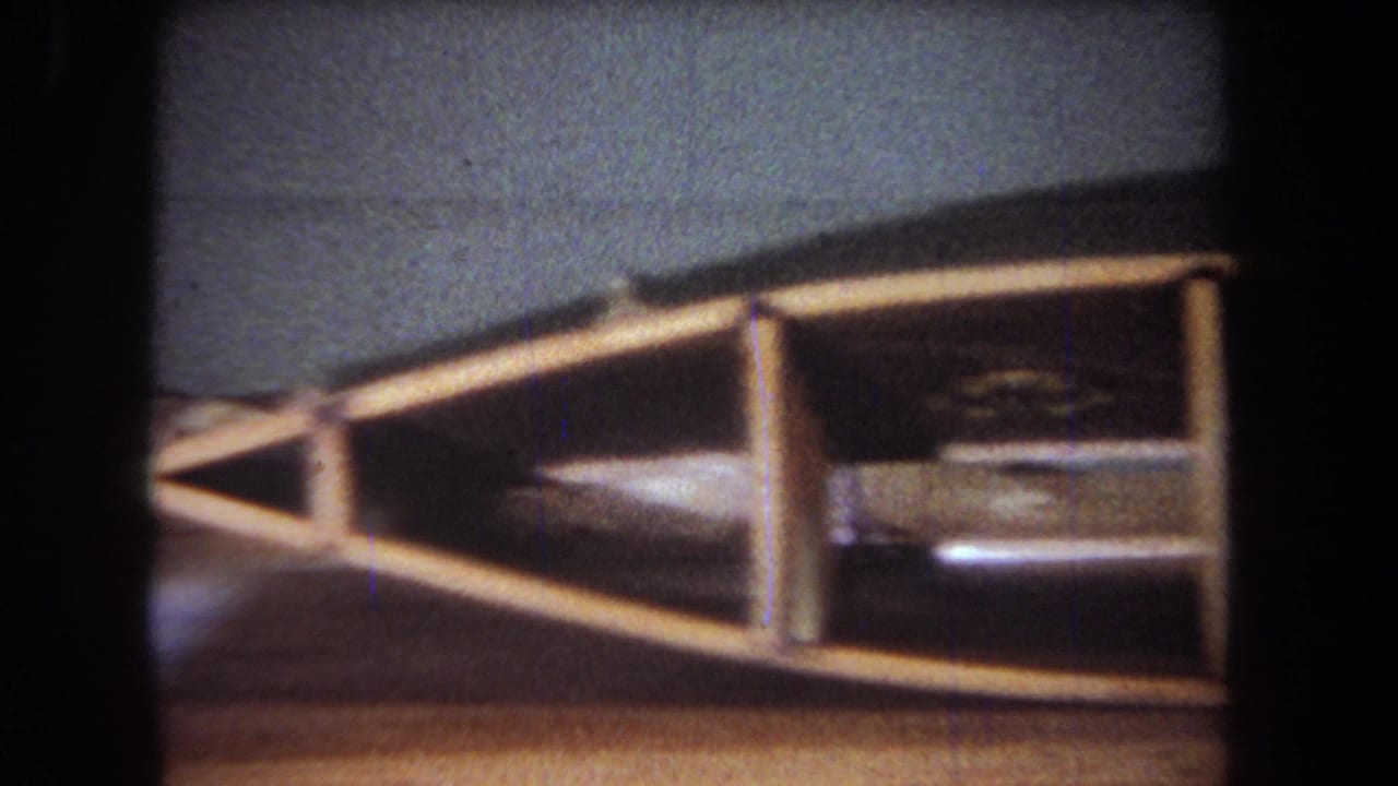 1965 Yucaipa-area home-movie frame showing a wooden craft or workshop structure on a table under low indoor light.
