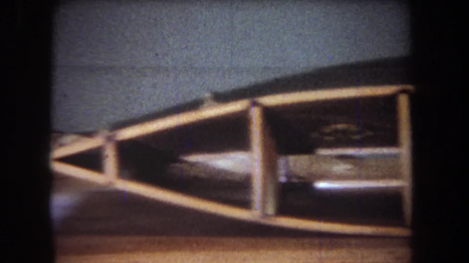 1965 Yucaipa-area home-movie frame showing a wooden craft or workshop structure on a table under low indoor light.