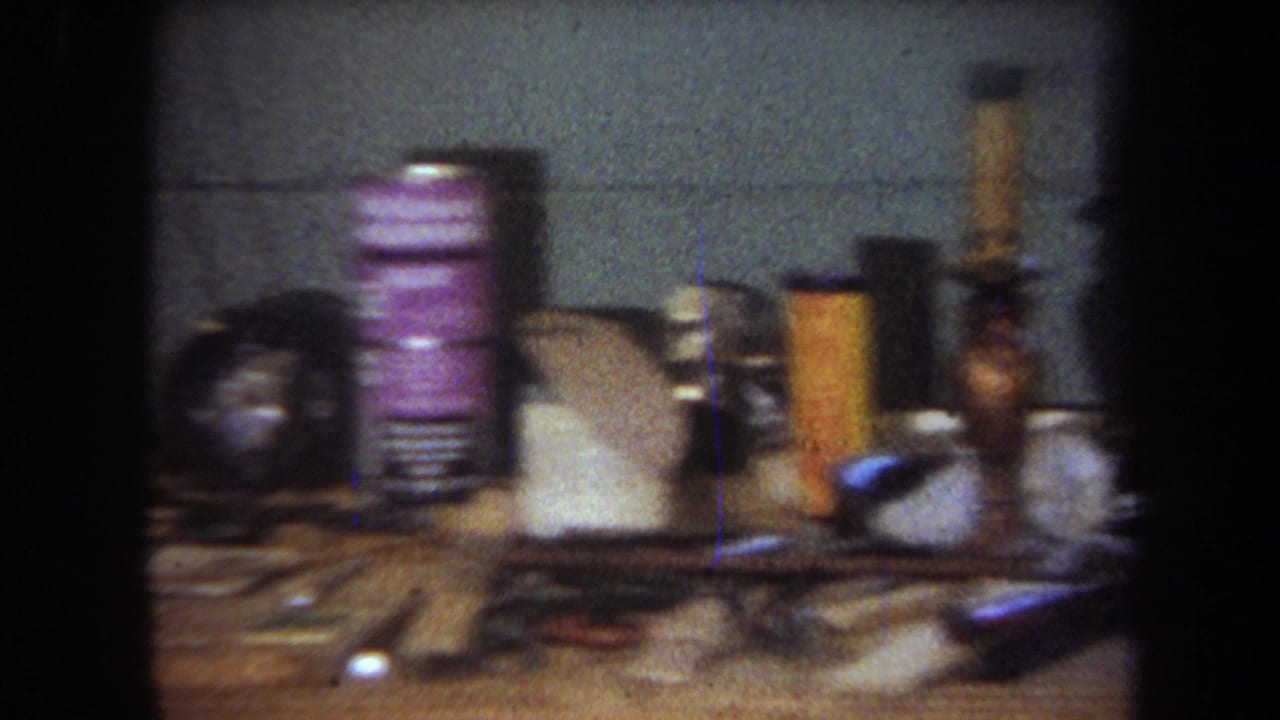 1965 8mm home-movie frame from Yucaipa showing a cluttered basement workbench with tools, cans, containers, and a gray block wall.