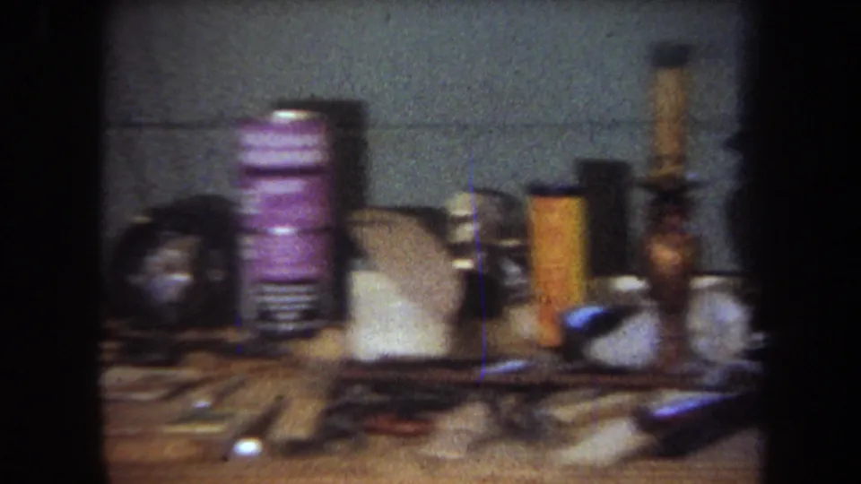 1965 8mm home-movie frame from Yucaipa showing a cluttered basement workbench with tools, cans, containers, and a gray block wall.