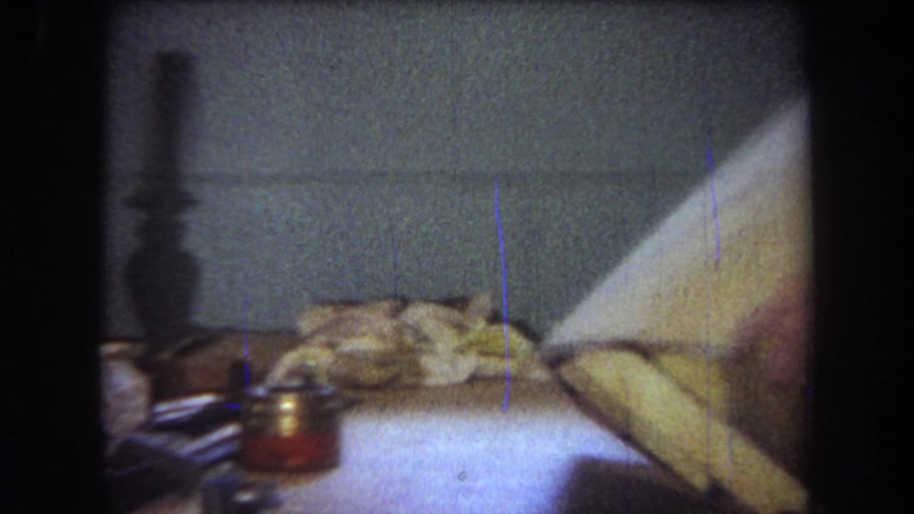 A large wood panel lies on a basement workbench in the 1965 Yucaipa home-movie footage, with tools and a small jar nearby.