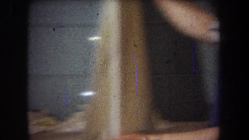 Soft, close 8mm frame showing a vertical piece of wood and partial movement of the man near the basement workbench.