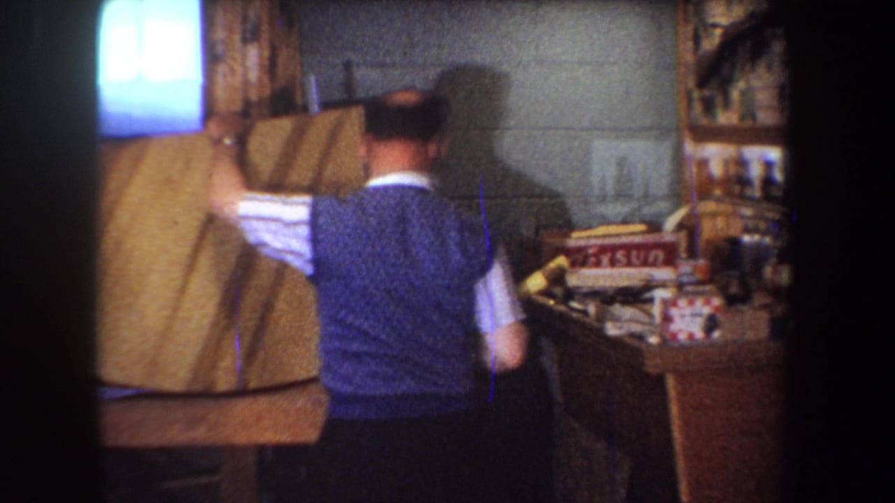 1965 Yucaipa workshop frame with a man turning a wood panel near shelves, supplies, and a visible Texsun box.