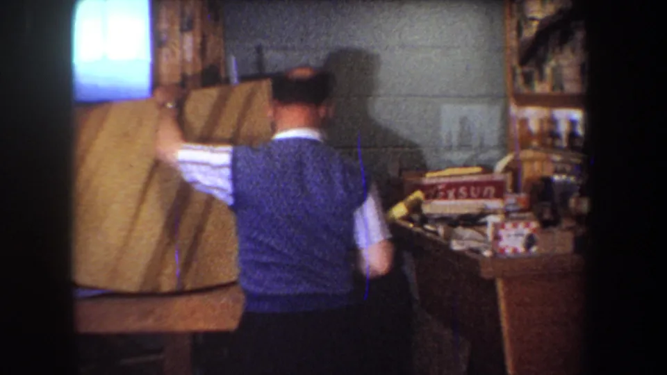 1965 Yucaipa workshop frame with a man turning a wood panel near shelves, supplies, and a visible Texsun box.