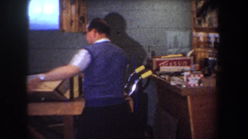 1965 Yucaipa basement workshop frame with the man at the bench near shelves, supplies, and a visible Texsun box.