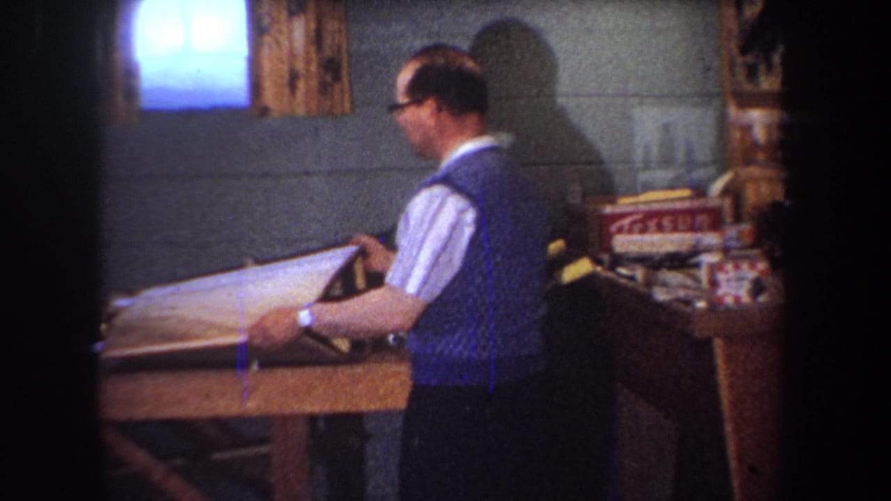 Man steadies a wooden or metal frame on a worktable.